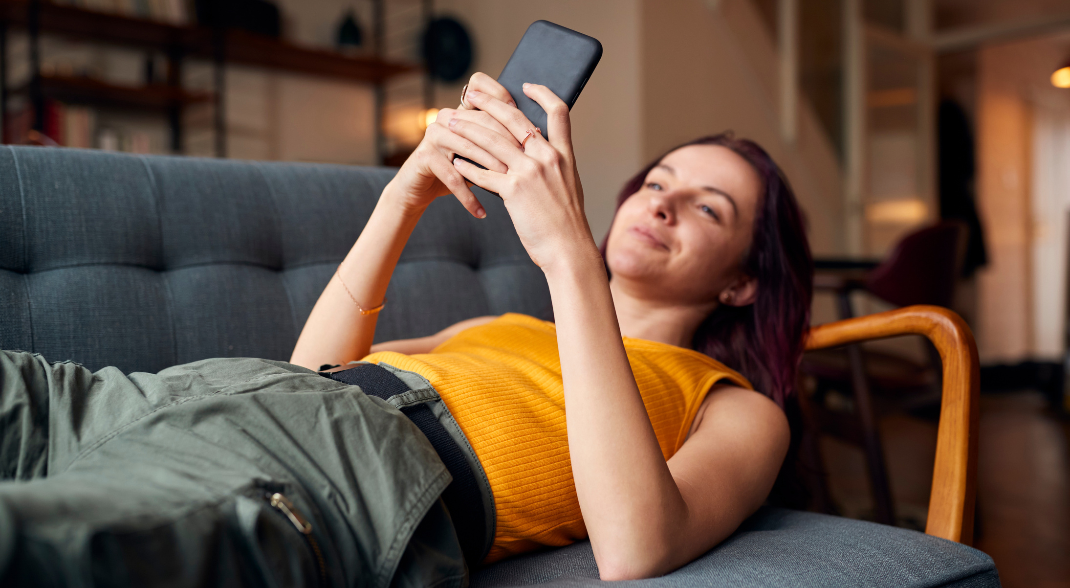 Young Woman Lying on Sofa at Home Looking at Mobile Phone Messag